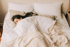 A lady with long dark hair is sleeping peacefully under a natural coloured organic cotton duvet 