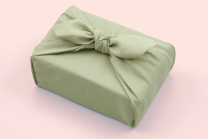 a gift wrapped up in green fabric and tied in a bow on a pink background 