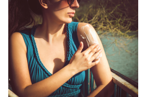 woman wearing blue top applying sunscreen to her arm