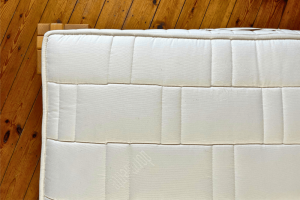 A natural mattress with undyed organic cotton cover quilted with organic wool on a wooden bed frame