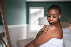 A woman is masssaging her shoulder while wearing a white organic cotton towel