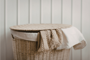 A wicker laundry basket with natural coloured clothing spilling out 