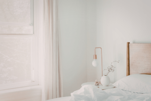 a bedroom with white walls, a large window and white curtains and white bedding 
