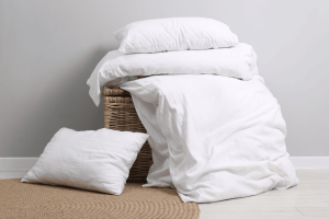 A stack of white organic cotton bedding next to a laundry basket 