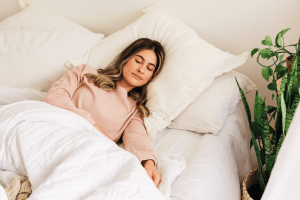 A woman sleeping peacefully in organic bedding, with green plants by the side of her bed 