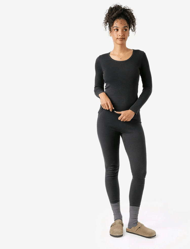 A woman with long hair wearing mauve organic cotton long johns and long sleeve vest with bare feet 