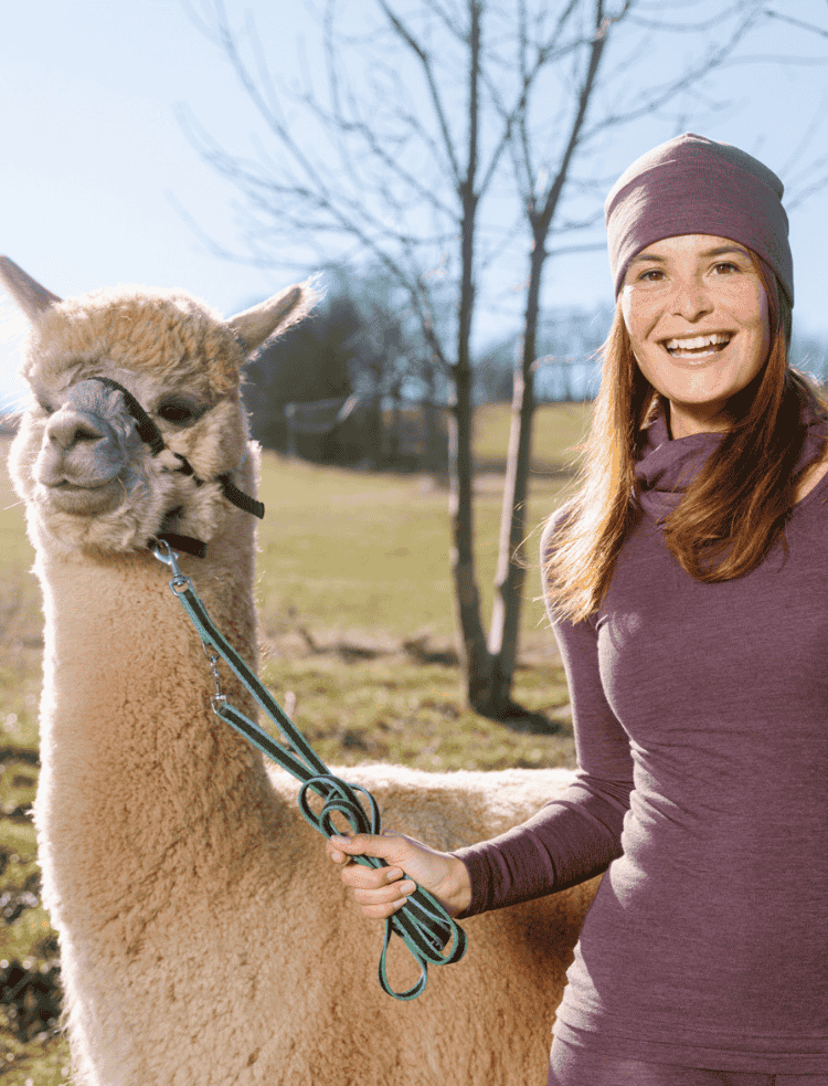 A woman wearing an organic purple heather long sleeved vest smiling with an alpaca