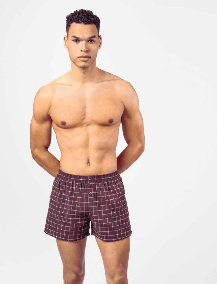 A man wearing burgundy organic cotton flannel boxer shorts with a light grey check pattern 