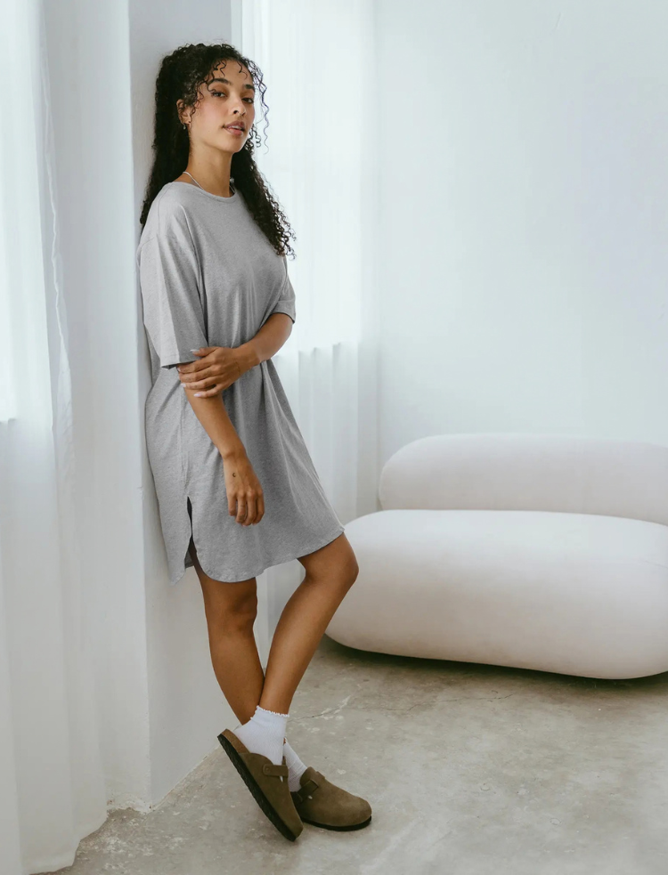 A woman is wearing a pink with white stripe organic cotton nightshirt 