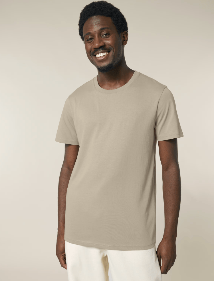 A man is wearing an organic cotton t-shirt in sand and smiling 