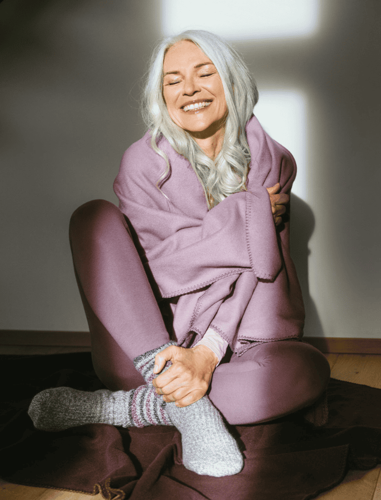 A lady wrapped in a mauve organic fleece blanket and mauve leggings 
