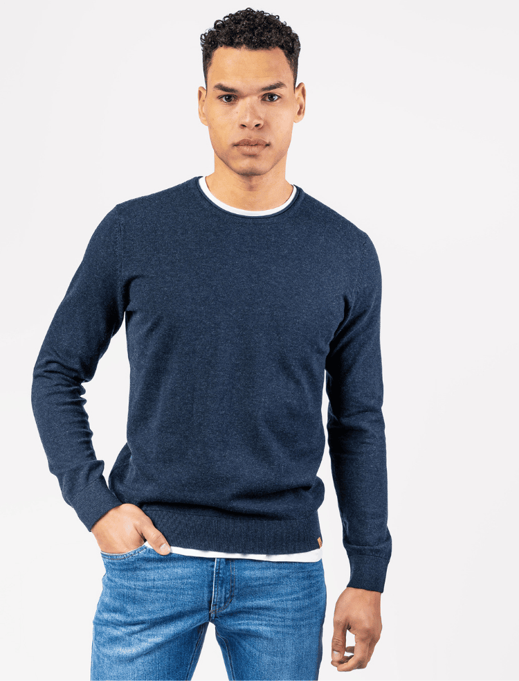 A man wearing a dark blue organic cotton and wool fine knit jumper and jeans, with his hand in his pocket
