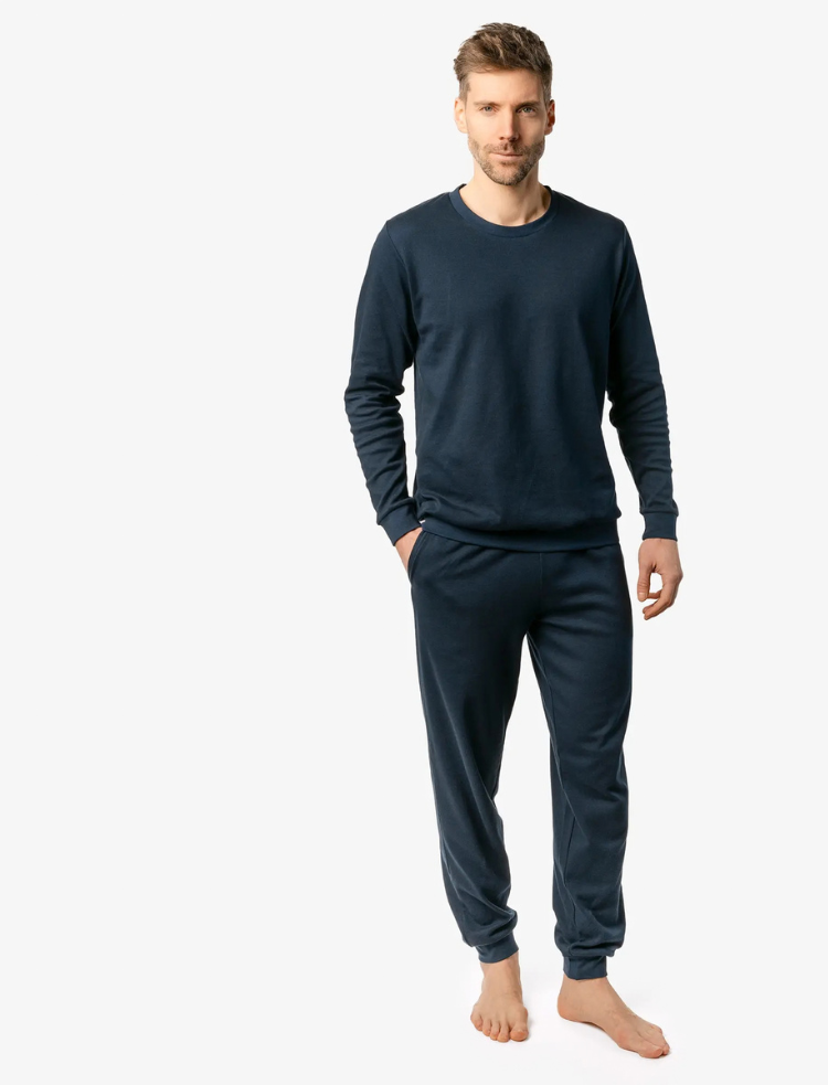 A man is wearing grey organic cotton check pyjamas and sitting on a wooden stool
