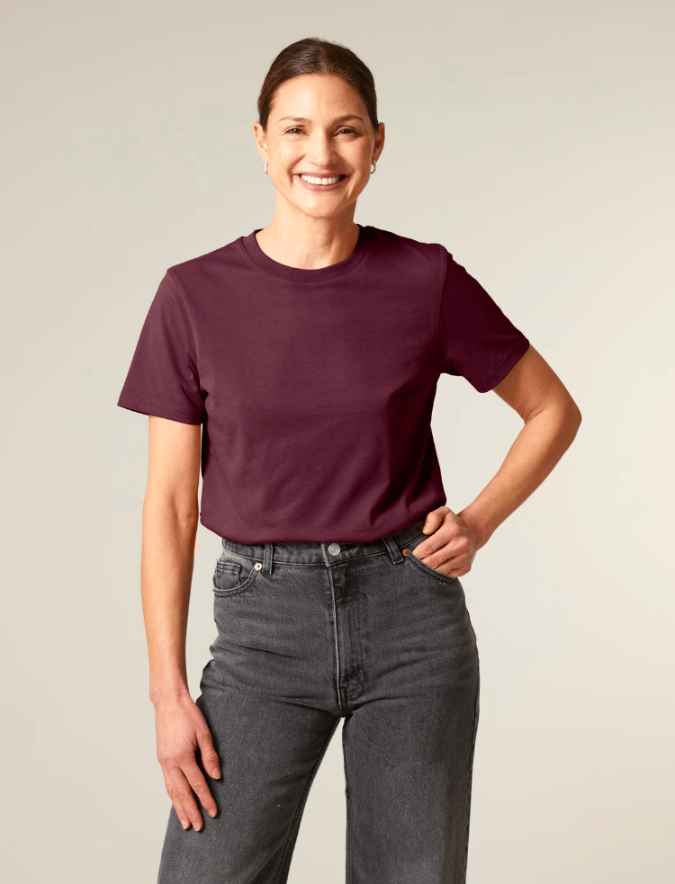 A woman is wearing organic cotton mulberry coloured t-shirt with her hand on her hip 