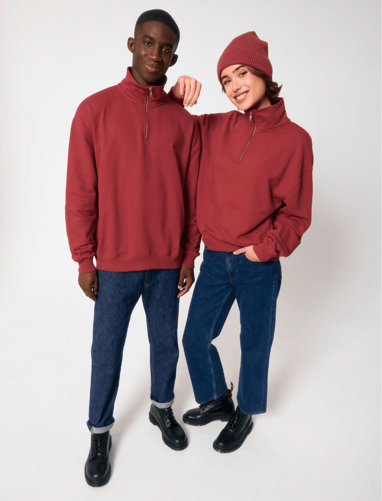 a man and a women wearing red organic cotton quarter zip sweatshirts and blue jeans 