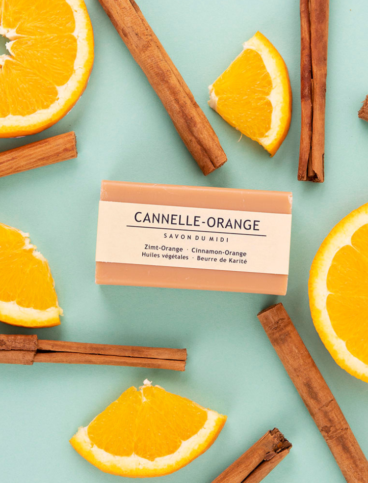 organic shea butter soap bar in cinnamon orange on a blue background with cinnamon sticks and orange slices