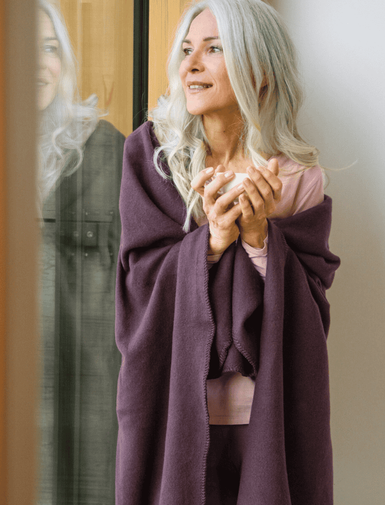 A lady wrapped in a mauve organic fleece blanket and mauve leggings 