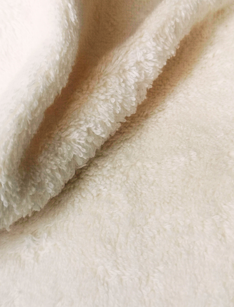 a folded up organic cotton shower towel, in a natural and undyed colour, with a cardboard swing tag printed with the Greenfibres logo 