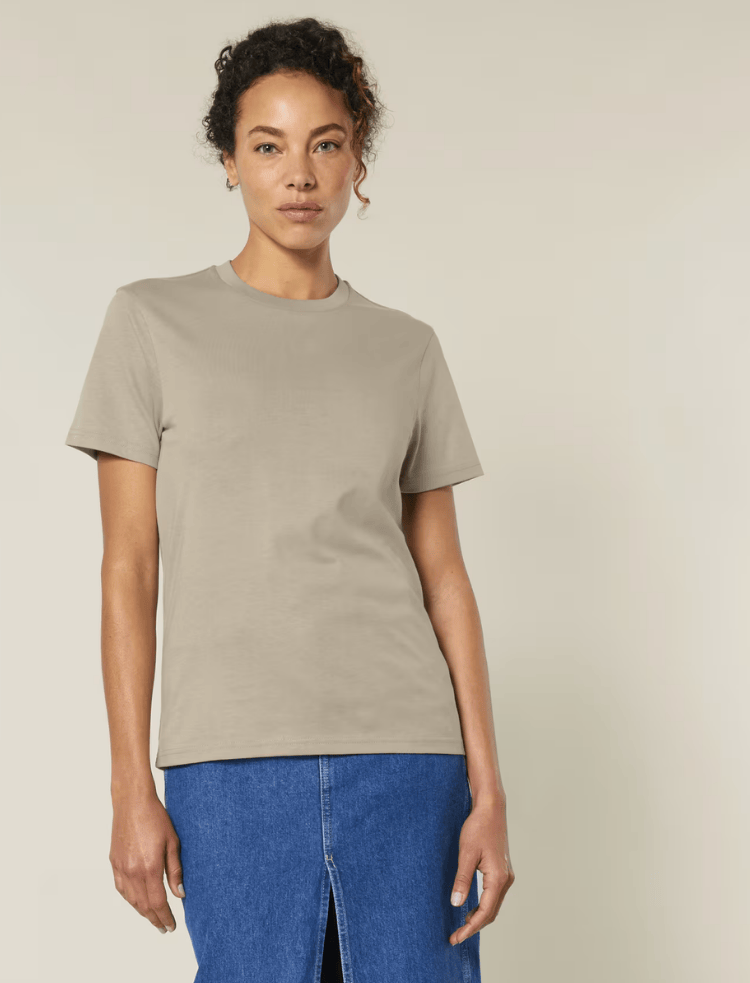 A man is wearing an organic cotton t-shirt in sand and smiling 