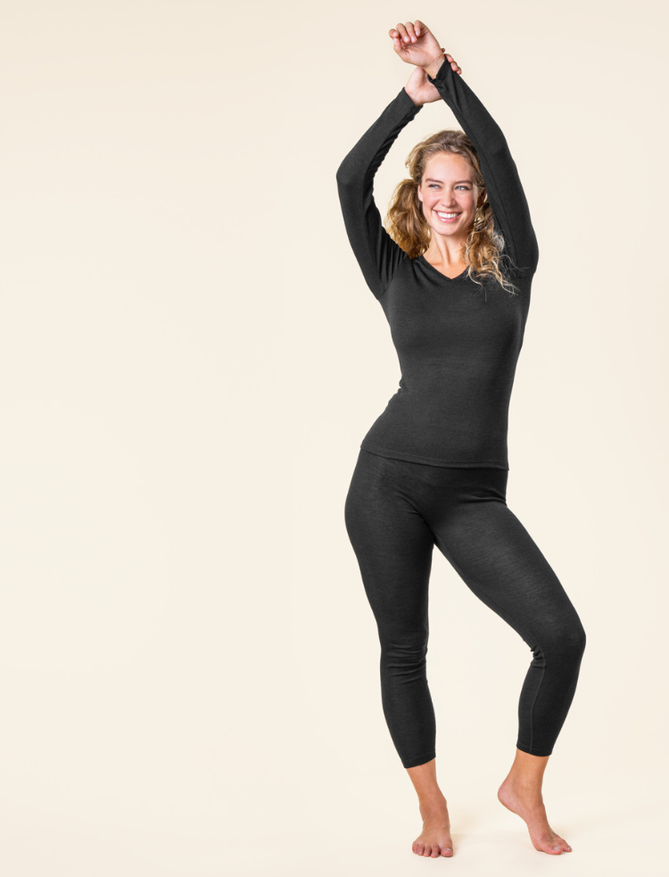 A lady with her hands above her head, wearing black organic merino wool and silk base layers 