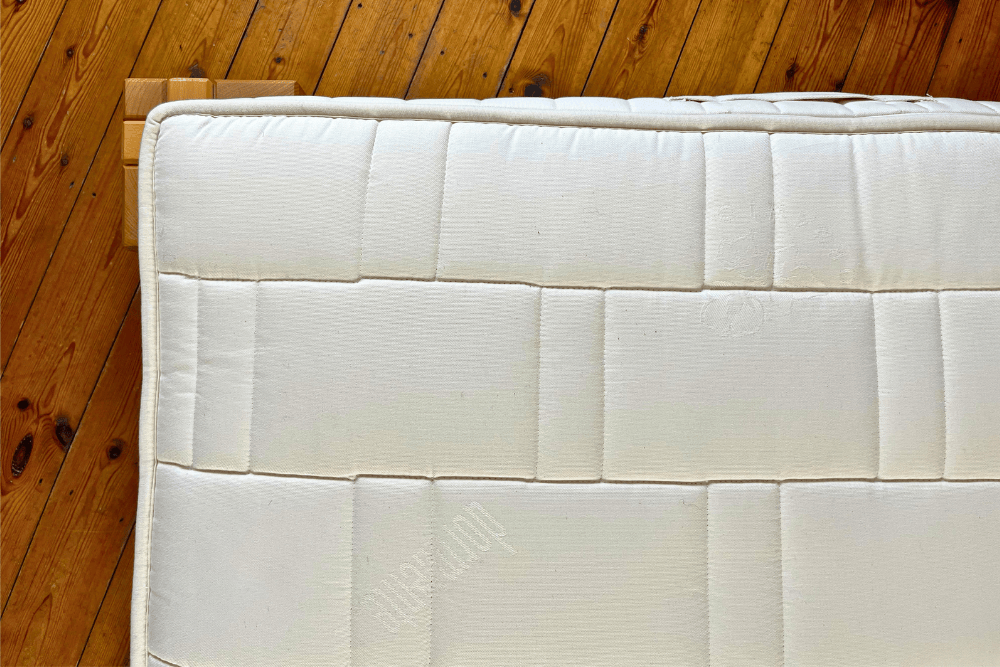 A natural mattress with undyed organic cotton cover quilted with organic wool on a wooden bed frame