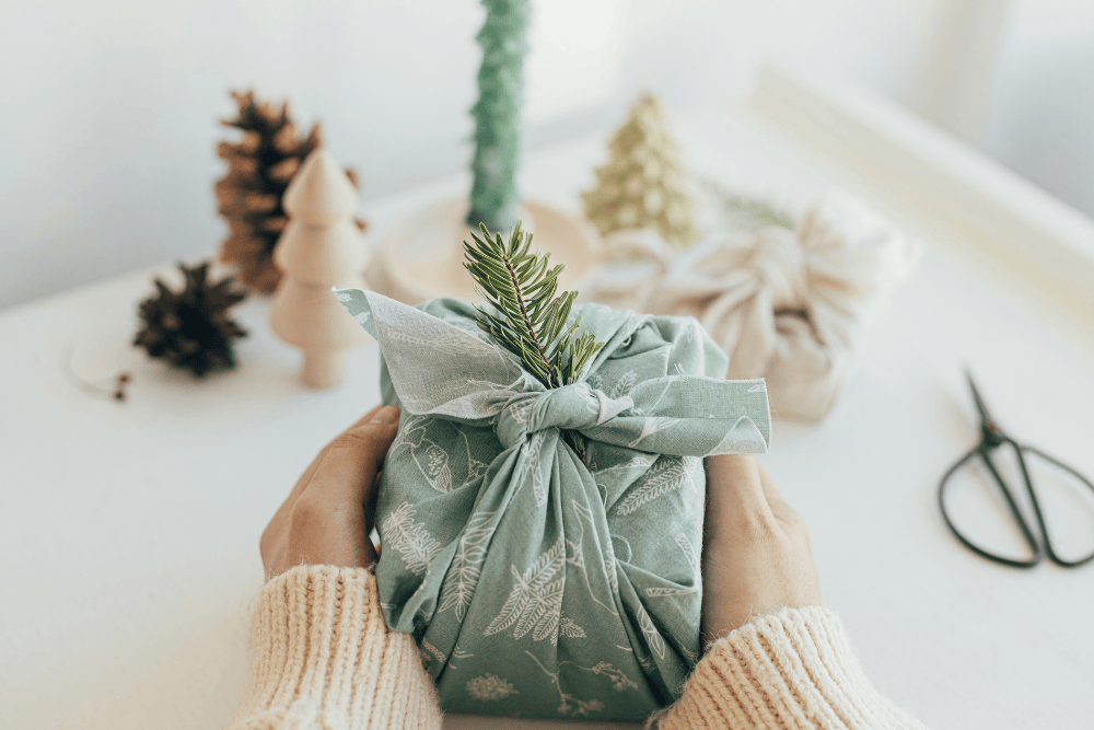 Hands holding a gift wrapped in green fabric with a sprig of rosemary 