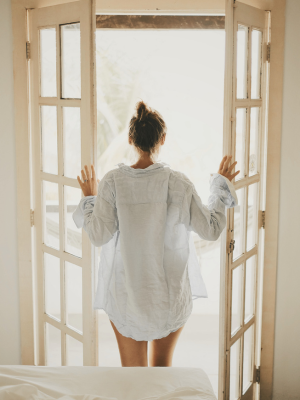 a woman is standing in front of an open window in a white shirt