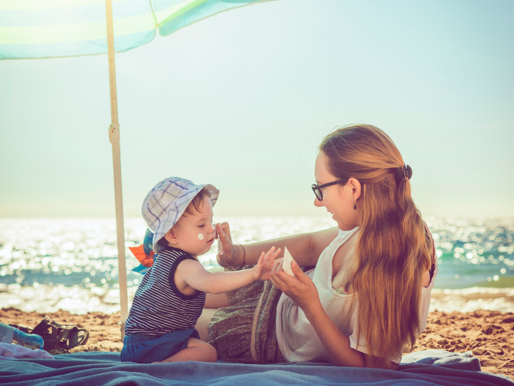 mother and baby on a beach under a sun umbrella using organic sunscreen