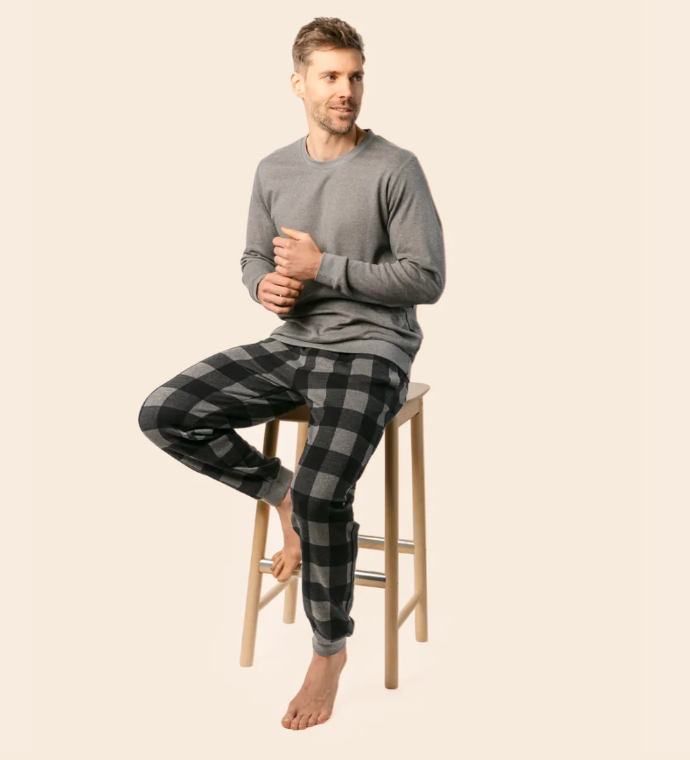 a man is wearing a long sleeve grey t-shirt with black and grey check pyjama trousers