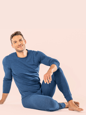 a man wearing mid blue organic cotton and wool base layers and sitting on the floor