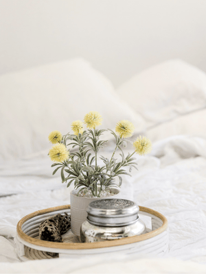 yellow flowers in a vase on a tray on a white duvet