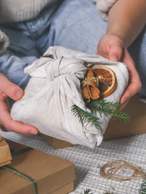 hands holding a christmas gift wrapped in natural fabric